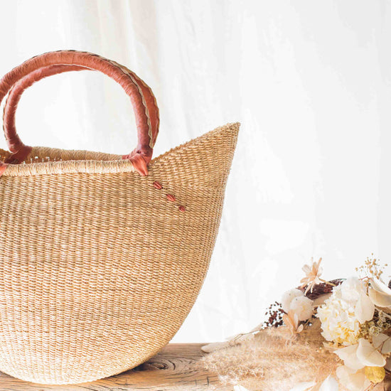 Woven straw bag with pink handles on a wooden surface with flowers and crystals.