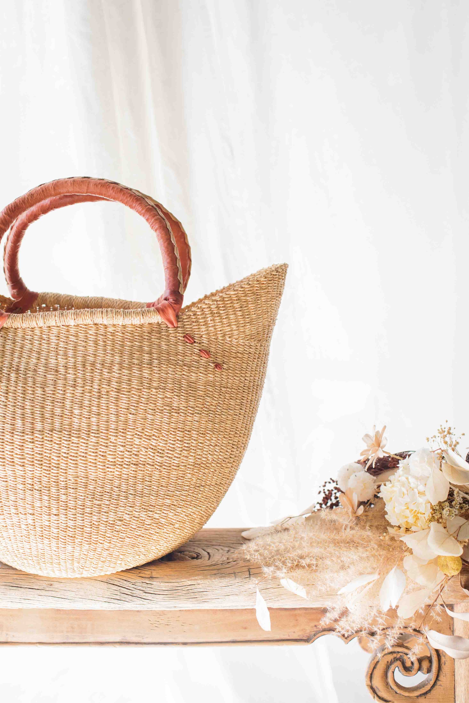 Woven straw bag with pink handles on a wooden surface with flowers and crystals.